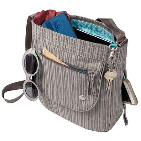 A gray striped JAUNT HK by Haiku with a roomy main compartment and toggle-locking zipper features an exterior pocket holding sunglasses, keys, a phone, a folded magazine, and a blue textile item—perfect for travel.