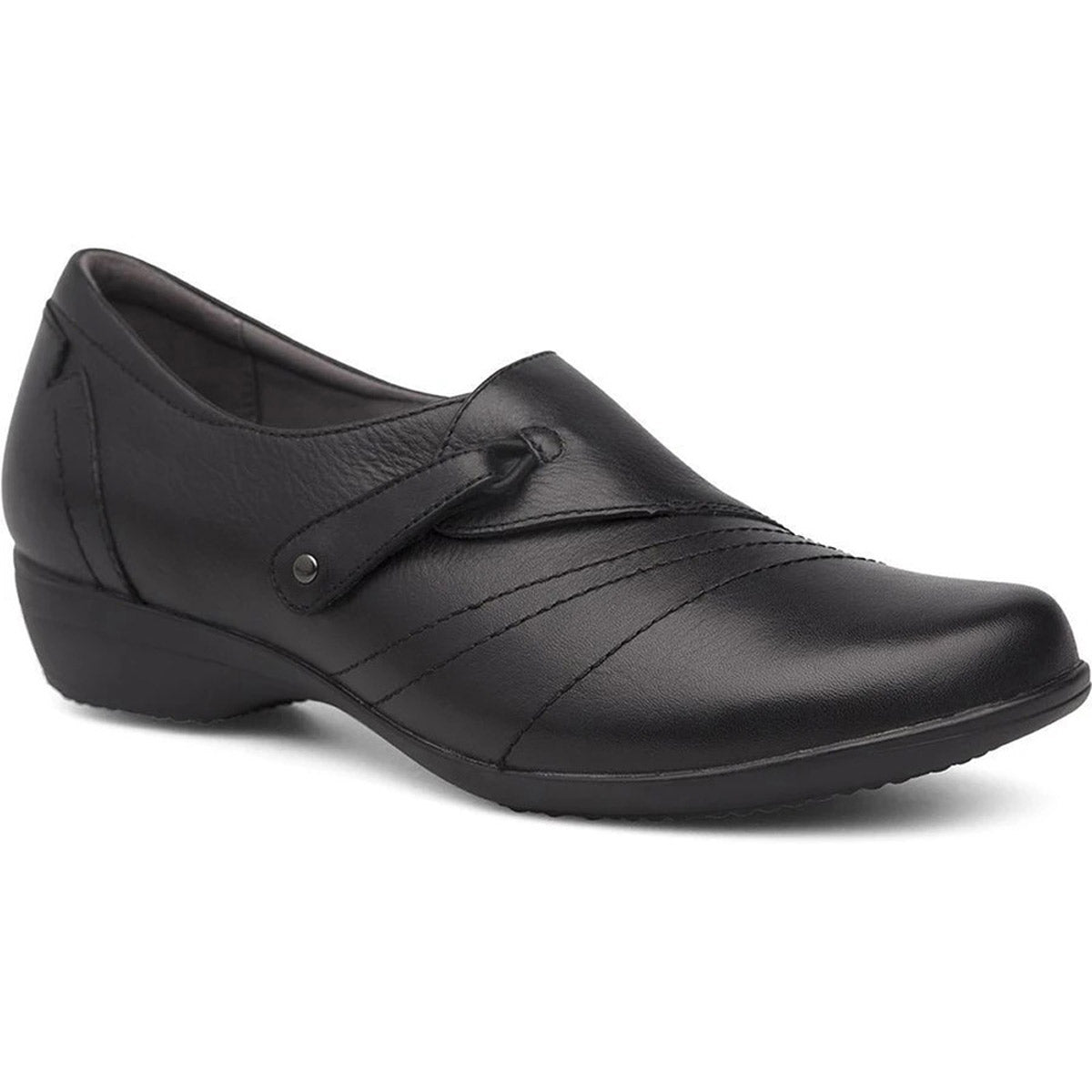 The Dansko DANSKO FRANNY MILLED NAPPA BLACK - WOMENS is a black leather slip-on shoe with a low heel, decorative stitching, and an adjustable hook and loop instep closure.