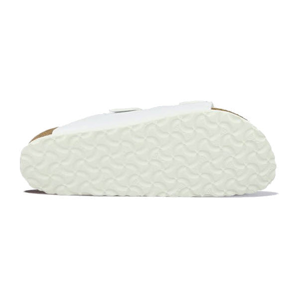 Bottom view of a white Birkenstock BIRKENSTOCK ARIZONA WHITE BIRKOFLOR - WOMENS sandal with a textured sole. The sole features a wavy pattern for traction, and the sandal showcases an anatomically shaped footbed along with its signature two-strap design.