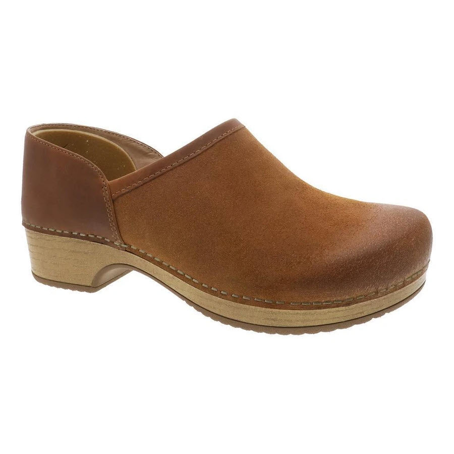 A brown leather clog with a low wood-like heel and closed toe, the Dansko DANSKO BRENNA TAN BURNISHED SUEDE - WOMENS is the perfect comfortable casual shoe for any occasion.