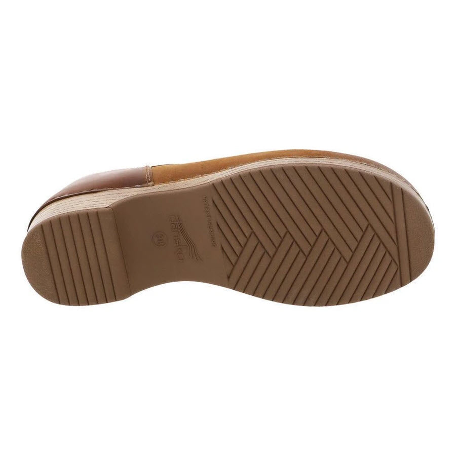 The image shows the bottom sole of a brown, comfortable casual shoe with herringbone and linear tread patterns, labeled &quot;Dansko DANSKO BRENNA TAN BURNISHED SUEDE - WOMENS.