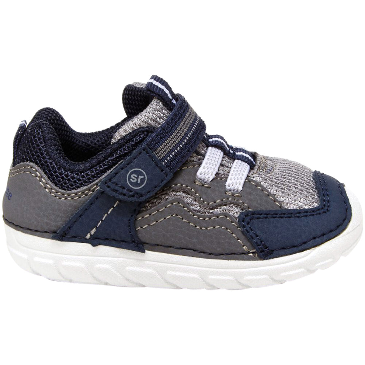 Introducing the Stride Rite SM Kylo Navy/Grey toddler sneaker. This stylish shoe features blue, gray, and white details with a convenient Velcro strap for effortless fastening. The mesh upper ensures breathability, while the cushioned white sole provides exceptional comfort. Designed with a slip-resistant sole, it guarantees stability during playtime.