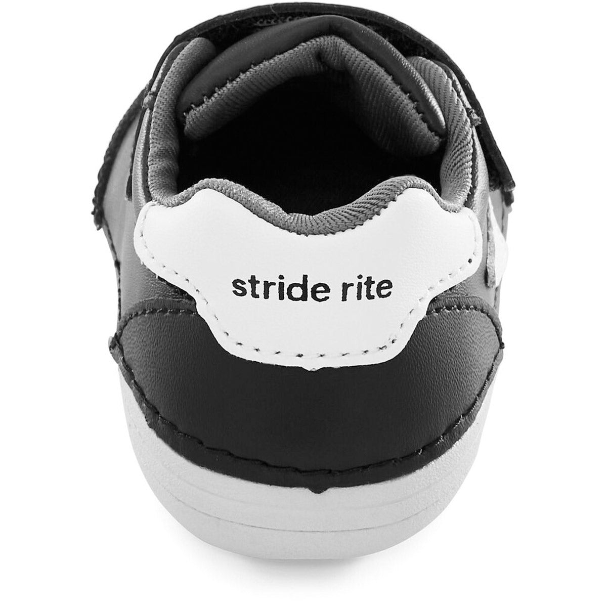 Close-up of the heel of a black and white kids&#39; athletic shoe, the STRIDE RITE SM KENNEDY BLACK - KIDS, with the brand name &quot;Stride Rite&quot; written on the back.