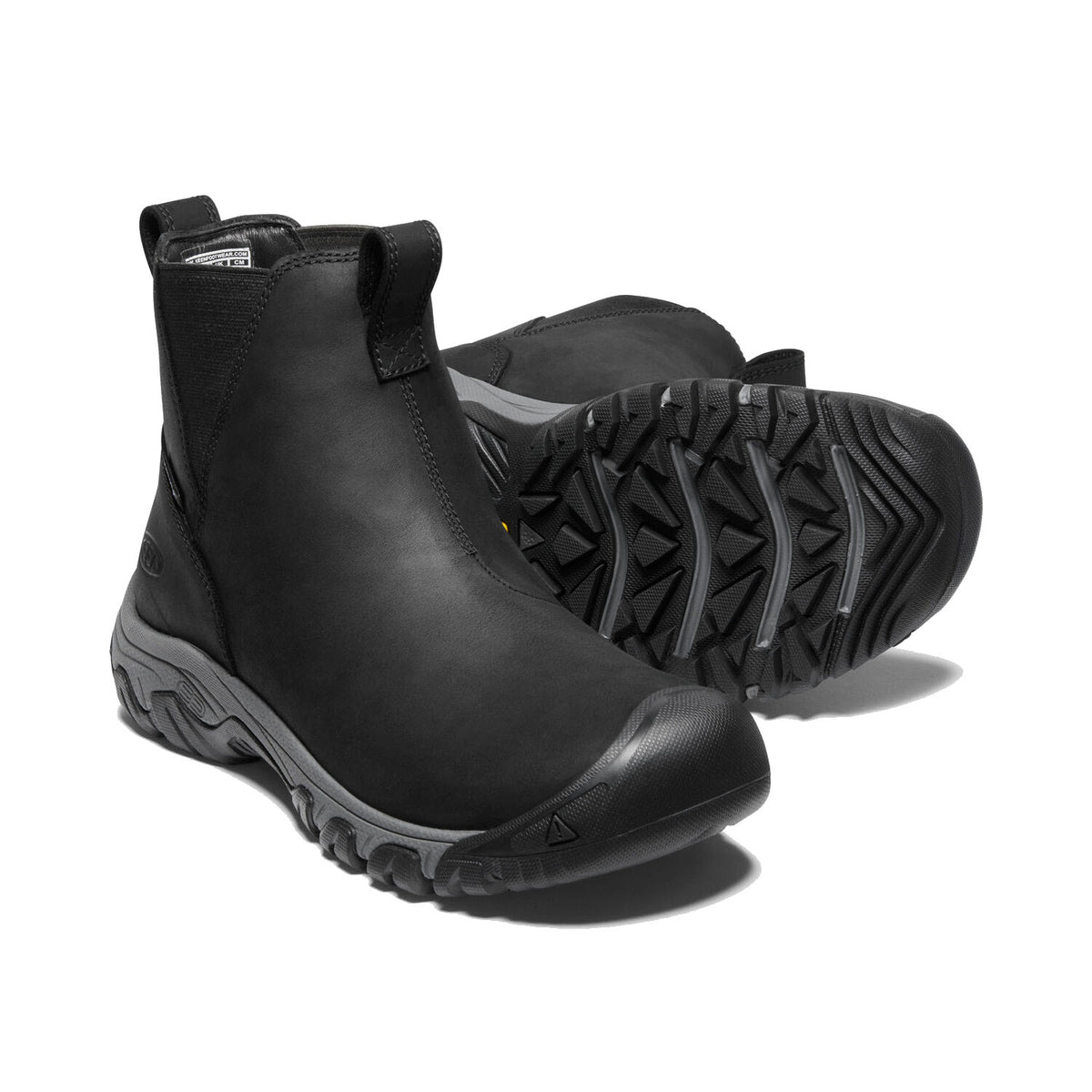 A pair of KEEN GRETA BLACK/STEEL GREY - WOMENS slip-on ankle boots by Keen, featuring rugged, textured soles and KEEN.WARM insulation, displayed against a white background.