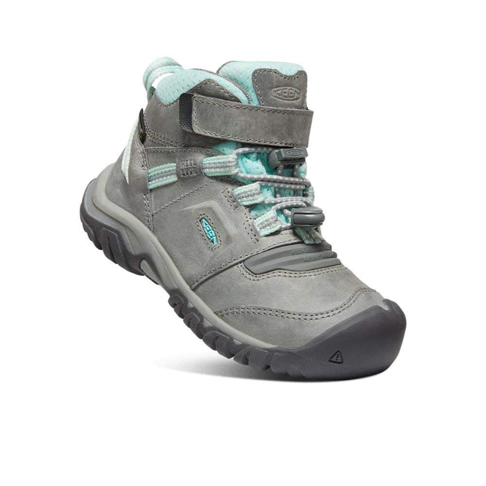 The Keen KEEN RIDGE FLEX MID CHILD GREY/BLUE TINT - KIDS in gray and teal features a rugged sole, ankle support, and is secured by laces, a velcro strap, and a convenient pull-cinch closure. A padded collar ensures extra comfort for little adventurers.