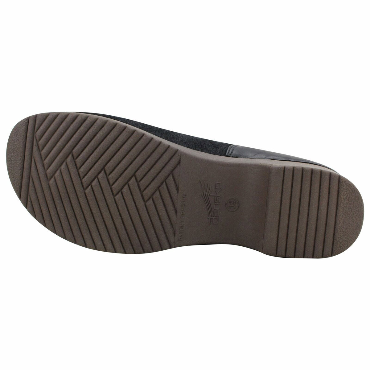 The image shows the bottom sole of a black slip-on shoe with a patterned tread and a small circular brand logo near the heel, highlighting the Dansko Brenna Black Burnished Suede - Womens design as comfortable casual footwear.