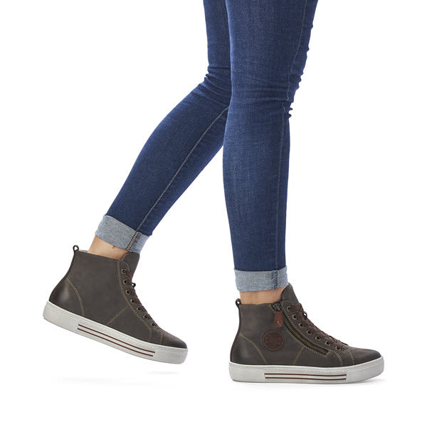 A person wearing rolled-up blue jeans and Remonte REMONTE WOOL LINED HIGH TOP SMOKE - WOMENS sneakers with dark nubuck leather and white soles, walking on a white background.