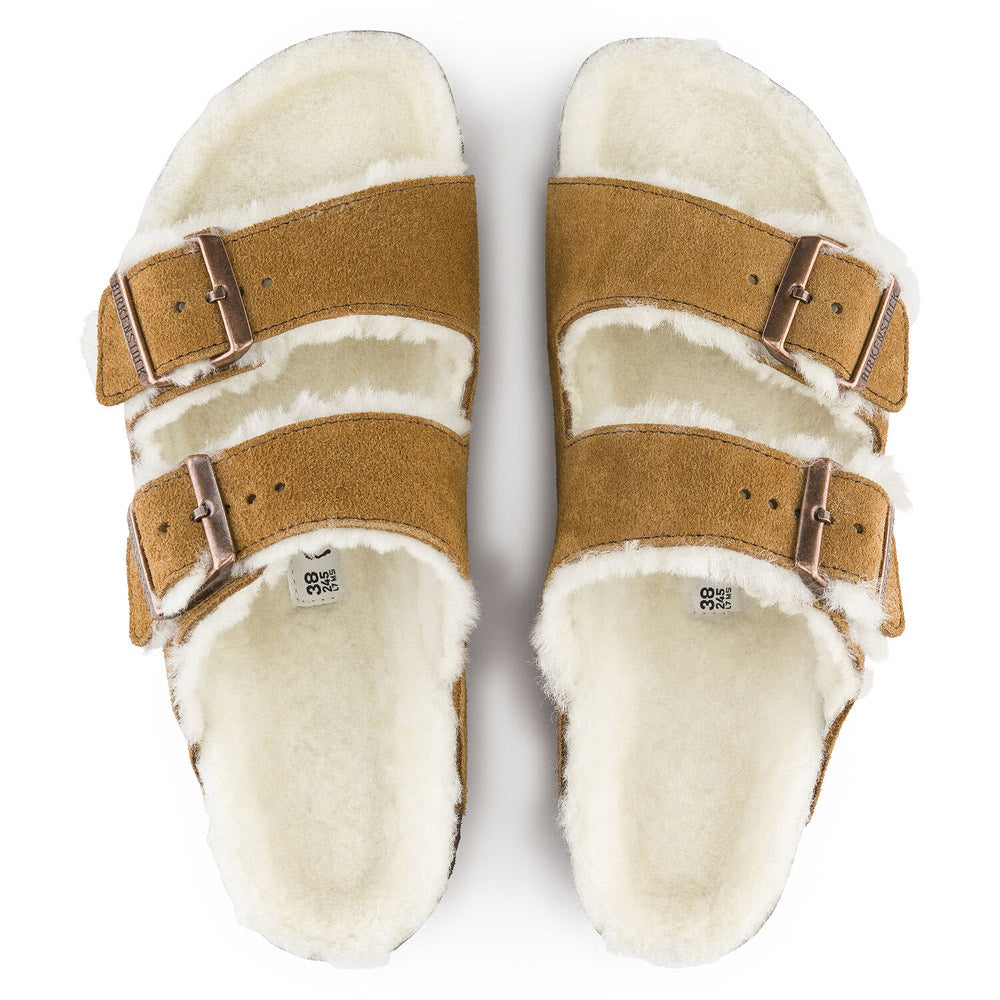 The BIRKENSTOCK ARIZONA SHEARLING MINK for women by Birkenstock is a pair of brown suede sandals with white fleece lining, featuring two adjustable straps with metal buckles and an anatomically formed cork-latex footbed.