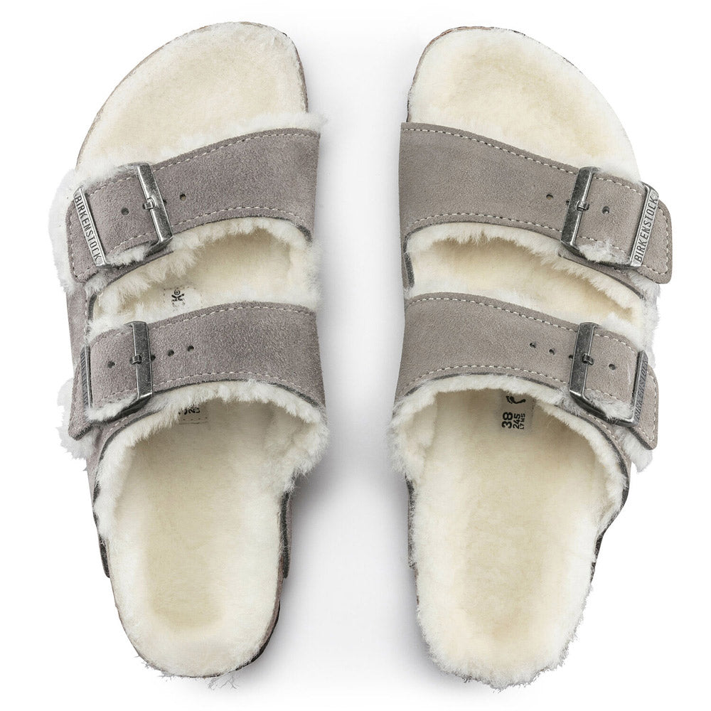 A pair of Birkenstock Arizona Shearling Stone Coin sandals for women, featuring grey suede with white shearling lining, two adjustable straps with metal buckles, and an anatomically formed footbed for ultimate comfort.