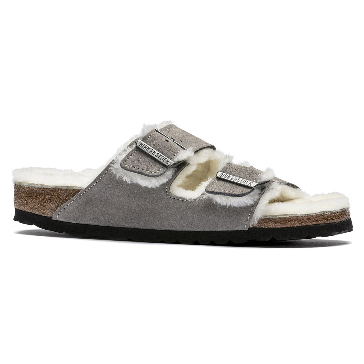 The BIRKENSTOCK ARIZONA SHEARLING STONE COIN slide sandal for women features a grey color with a white fur lining, dual adjustable straps, and a cork and rubber sole. It is designed with an anatomically formed footbed crafted from genuine suede, providing exceptional comfort.