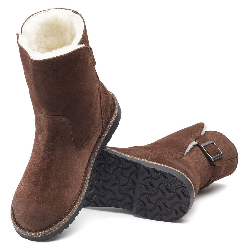 A pair of Birkenstock UPSALLA Shearling Espresso Suede boots for women with black rubber soles, fleece lining, and an adjustable strap on one boot.