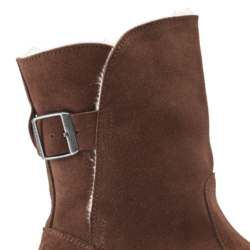 Close-up of a brown suede boot with a silver buckle and white fleece lining visible at the top edge, reminiscent of the comfortable design of the Birkenstock Upsalla Shearling Espresso Suede for women.