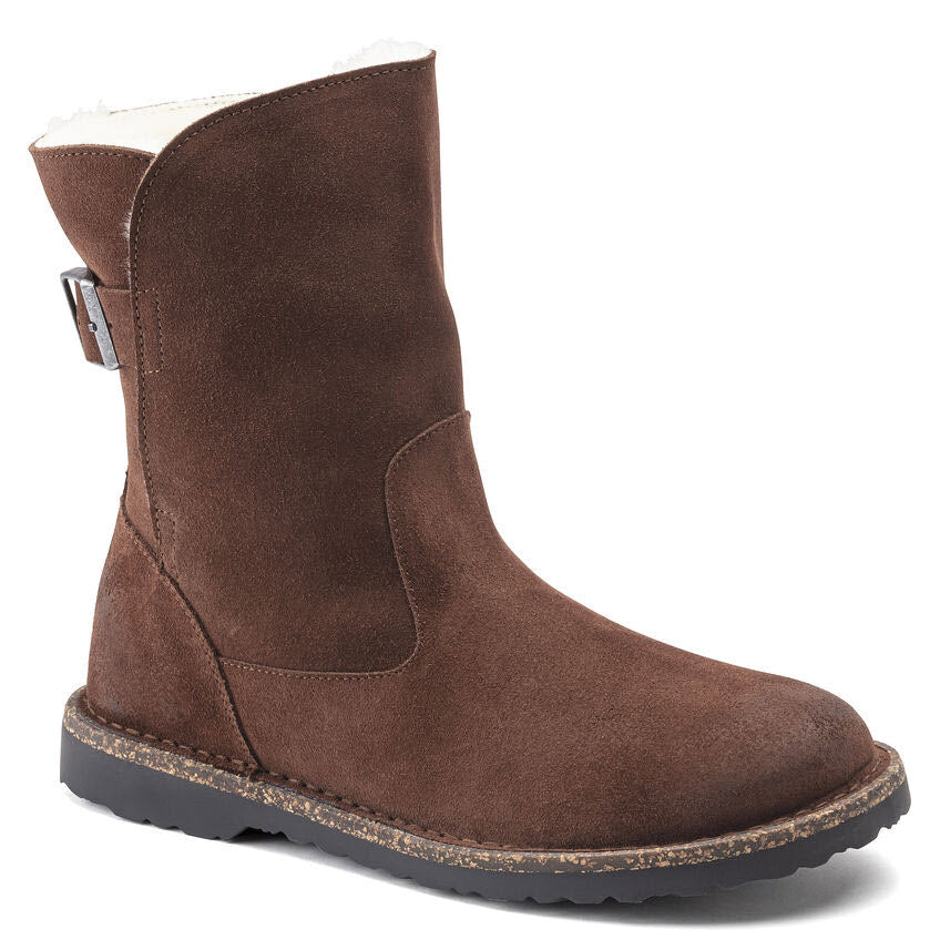 The BIRKENSTOCK UPSALLA SHEARLING ESPRESSO SUEDE for women features a brown, mid-calf suede boot with a black rubber sole, a buckle detail on the side, and a cozy cork-latex footbed for added comfort.