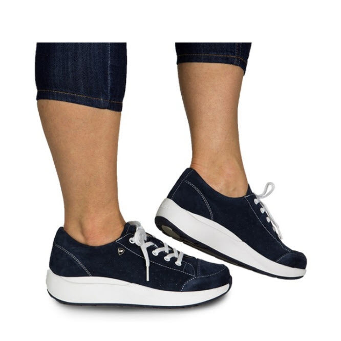 Individual wearing cropped jeans and navy blue Xelero Heidi Deep Ocean sneakers for women, featuring white soles and laces.