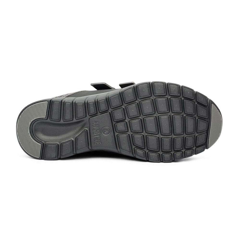 The bottom view of the ANODYNE SPORT JOGGER DOUBLE DEPTH BLACK/GREY - WOMENS shoe by Anodyne reveals a black sole with a ridged and patterned tread design, featuring various textured grip sections enhanced with extra depth for added traction.