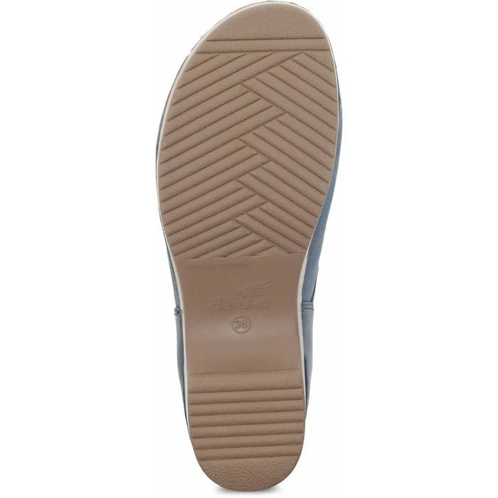 The image depicts the sole of the Dansko Brenna Navy Burnished slip-on shoe for women, showcasing a comfortable design with a textured pattern consisting of diagonal grooves and horizontal lines in tan, specifically engineered for enhanced odor control.