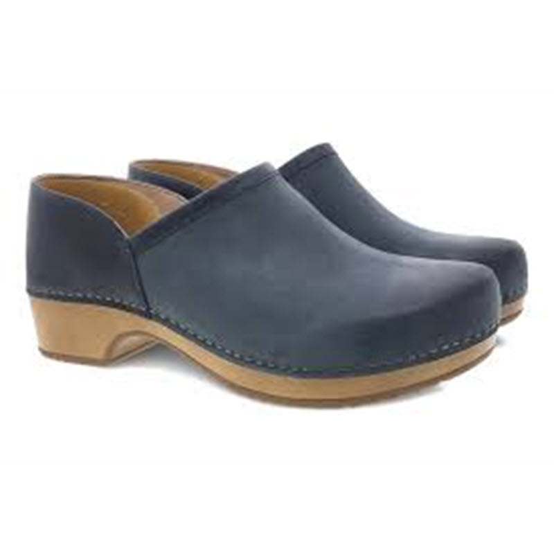 The DANSKO BRENNA NAVY BURNISHED - WOMENS clogs by Dansko feature navy blue uppers with tan wooden soles and a closed-back design, providing a comfortable slip-on shoe experience with enhanced odor control.