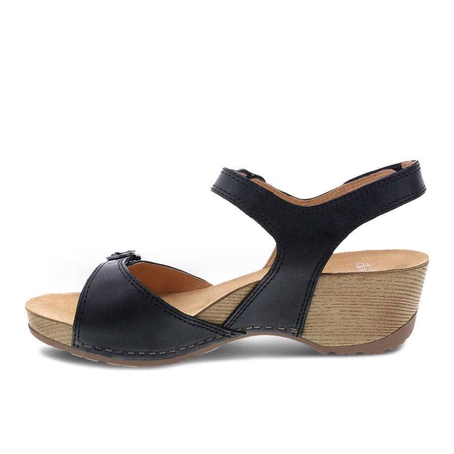 The Dansko Tricia Black Milled Burnished wedge sandal features leather uppers, a wooden sole, and an ankle strap designed for all-day comfort. These women&#39;s sandals are perfect for any occasion.