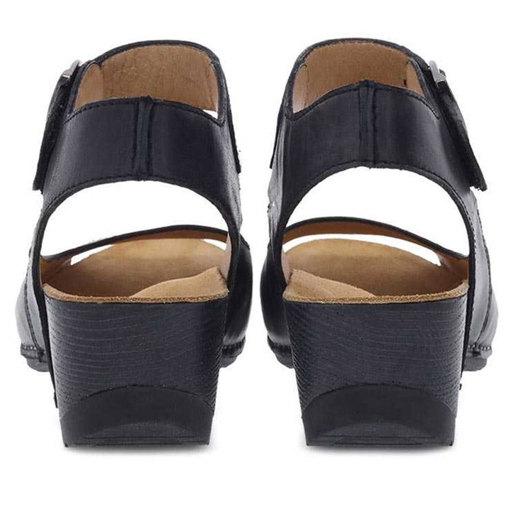 Revised Sentence: Rear view of a pair of Dansko Tiana Black Burnished shoes for women, featuring open-back design, black leather upper, low heels, and beige insoles—perfect for those seeking a comfy sandal.