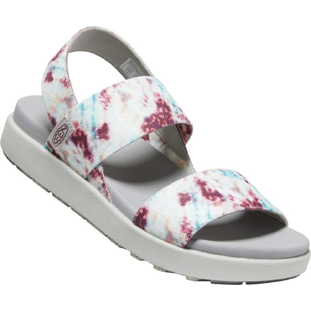 The KEEN Women&#39;s Elle Backstrap Andorra Tie Dye Sandal by Keen showcases a stylish white sandal with vibrant multi-colored tie-dye straps, a sleek grey sole, and an eco-friendly design. It also includes a cushioned footbed for enhanced comfort.