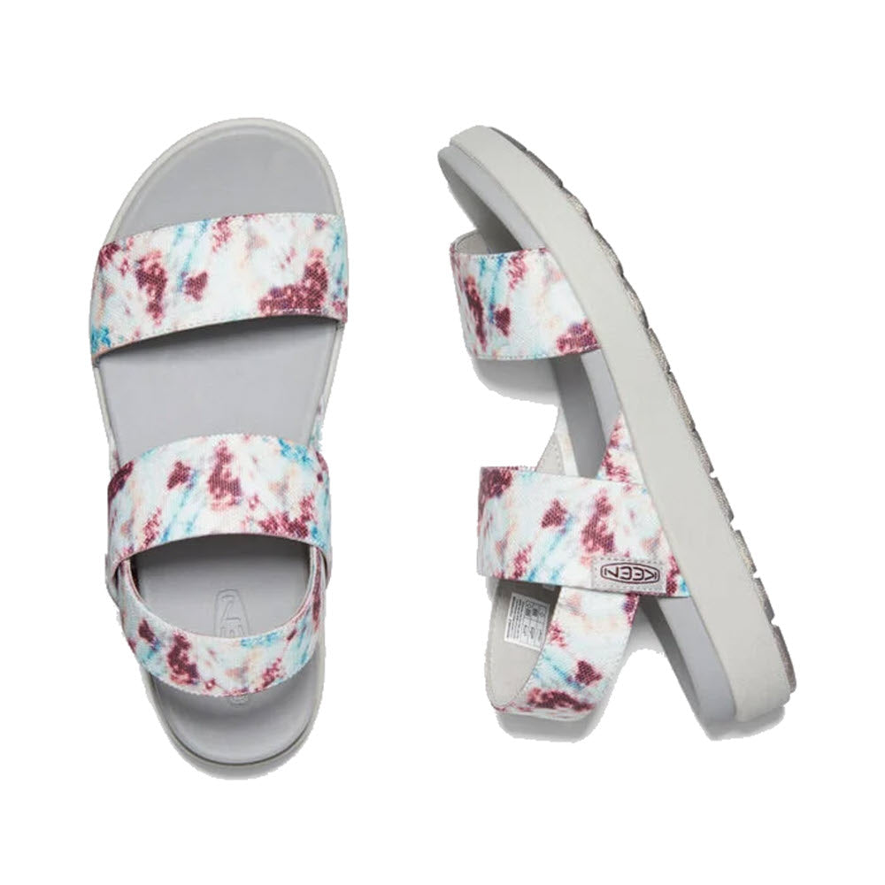 A pair of KEEN ELLE BACKSTRAP ANDORRA TIE DYE women&#39;s sandals, featuring open-toe design with pink, blue, and purple tie-dye straps and gray soles. These white and light blue eco-friendly sandals include a cushioned footbed for added comfort, shown from above and at an angle.