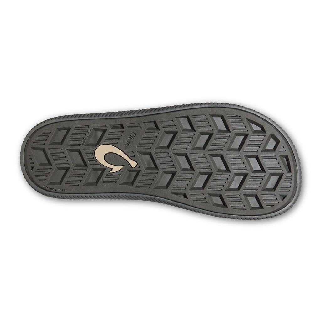 The bottom of the water-friendly OLUKAI ULELE DARK SHADOW - MENS sandal from Olukai features a textured, hexagonal pattern sole with a distinctive emblem in the center.