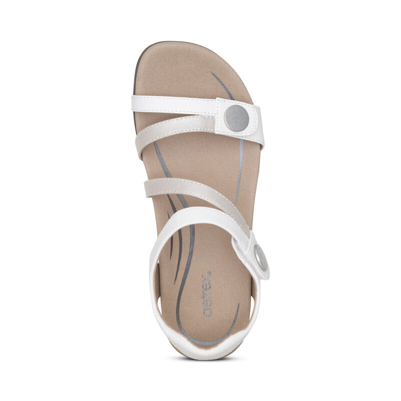 Top view of an Aetrex adjustable sandal with three straps and a circular decoration, featuring a tan memory foam footbed with gray stitching details for enhanced arch support. This is the AETREX JESS WHITE - WOMENS.