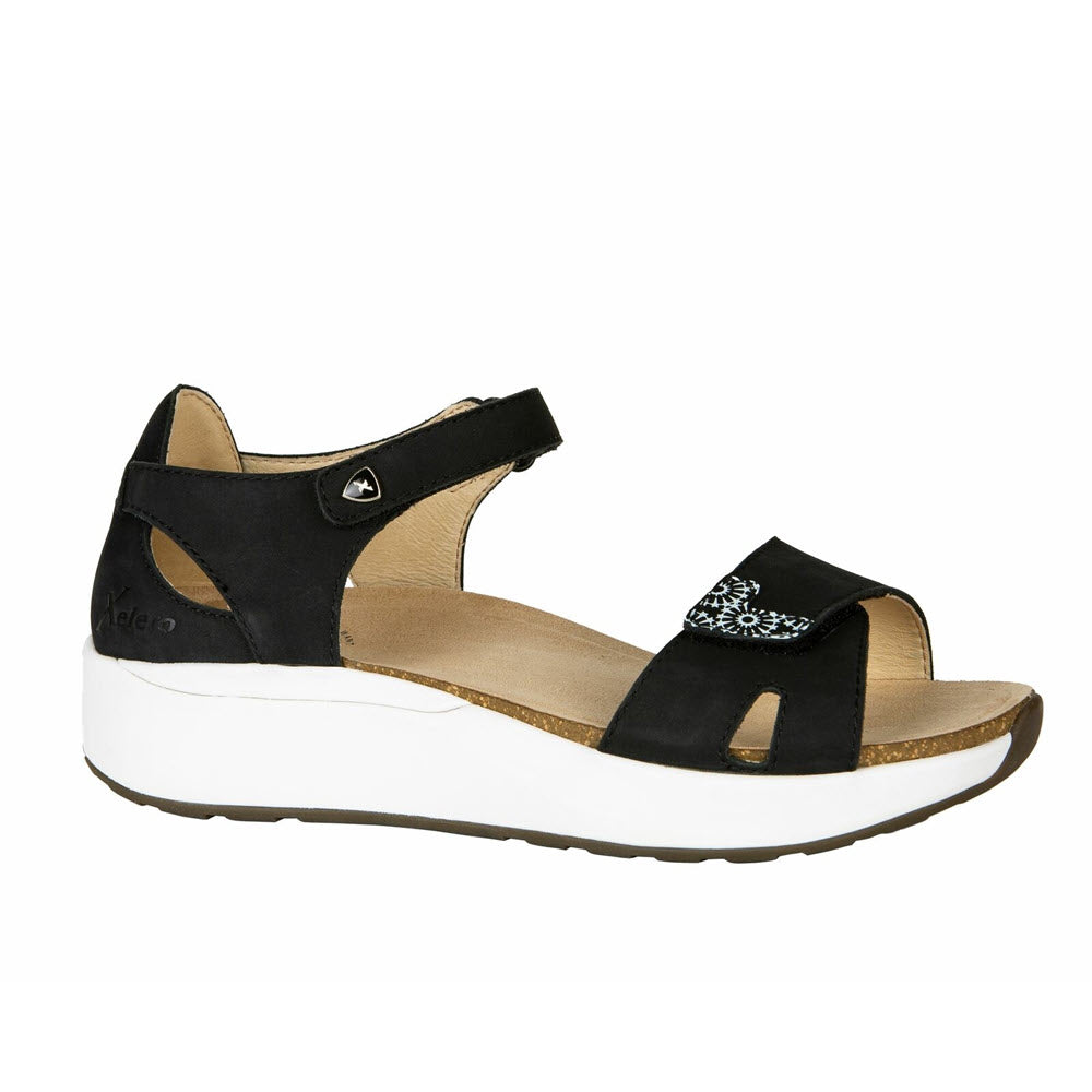 Introducing the Xelero Santorini Black Nubuck - Women&#39;s sandal: a stylish black open-toe design with an ankle strap and a sleek white sole. This elegant sandal features a small ornamental design on the upper strap, offering a touch of flair. With a cushioned footbed for maximum comfort and a slip-resistant sole for stable footing, it&#39;s perfect for every step you take.