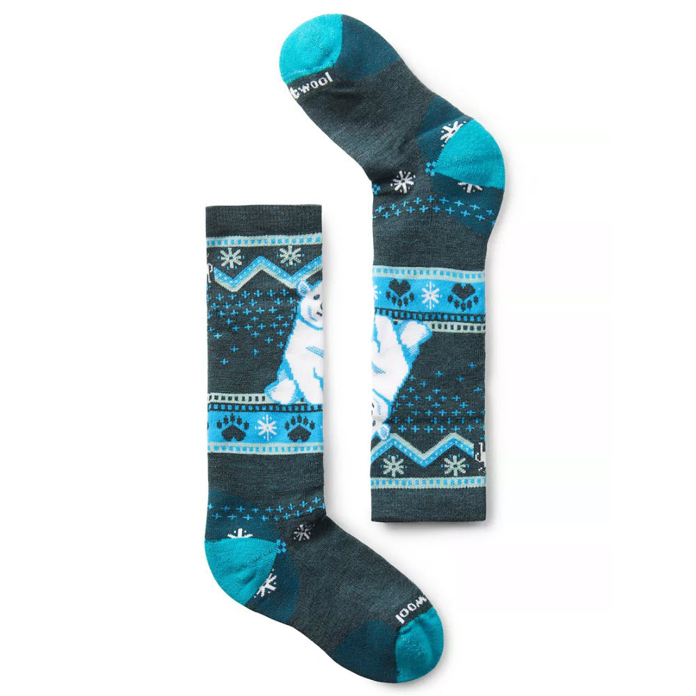 Pair of blue and gray SMARTWOOL WINTERSPORT KNEE HIGH SOCKS POLAR BEAR TWILIGHT BLUE - KIDS featuring a charming polar bear design and snowflake patterns. One Merino wool sock is laid flat while the other is placed sideways to display both the design and heel.