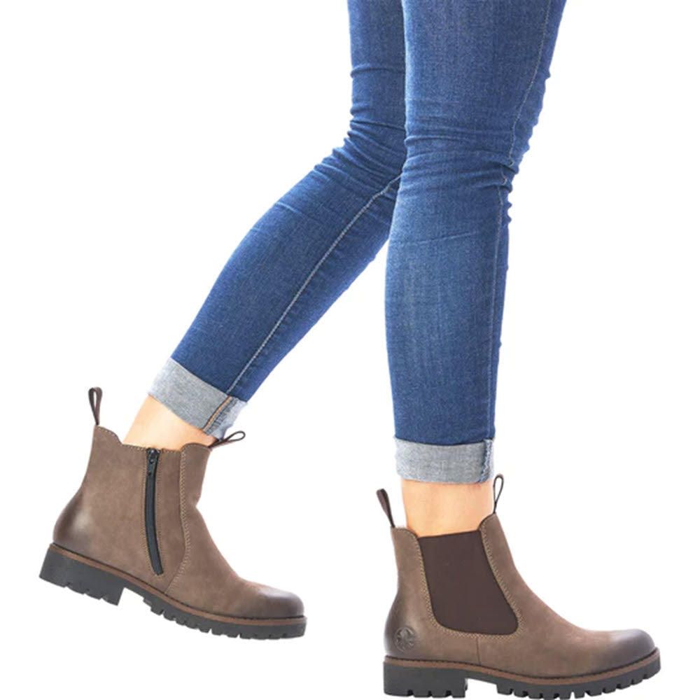 Person wearing the Rieker RIEKER LUG SOLE CHELSEA WITH ZIP MUD - WOMENS with side zippers and thick soles, paired with rolled-up blue jeans.