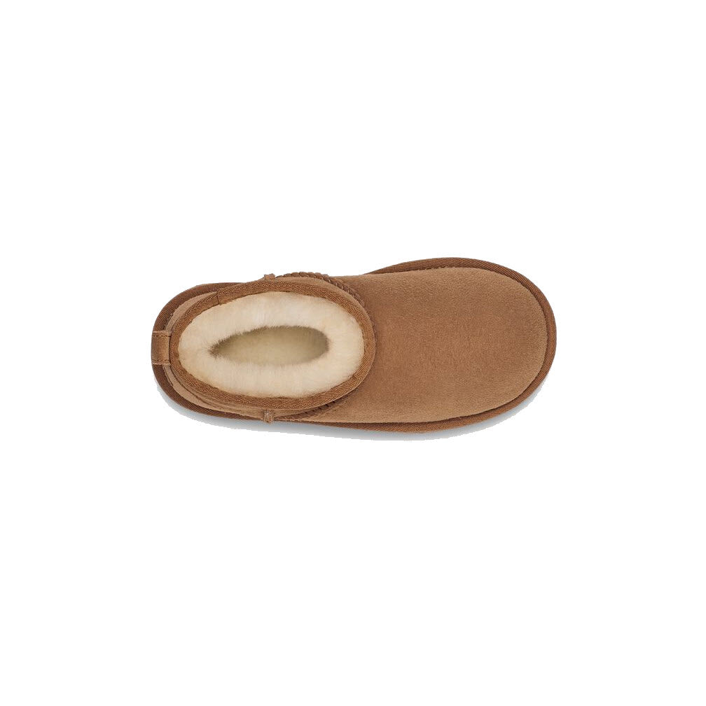 Top view of a single brown slipper with a soft white inner lining, designed for comfort and warmth, featuring an UGGplush™ insole from the Ugg brand&#39;s UGG CLASSIC ULTRA MINI CHESTNUT - KIDS collection.