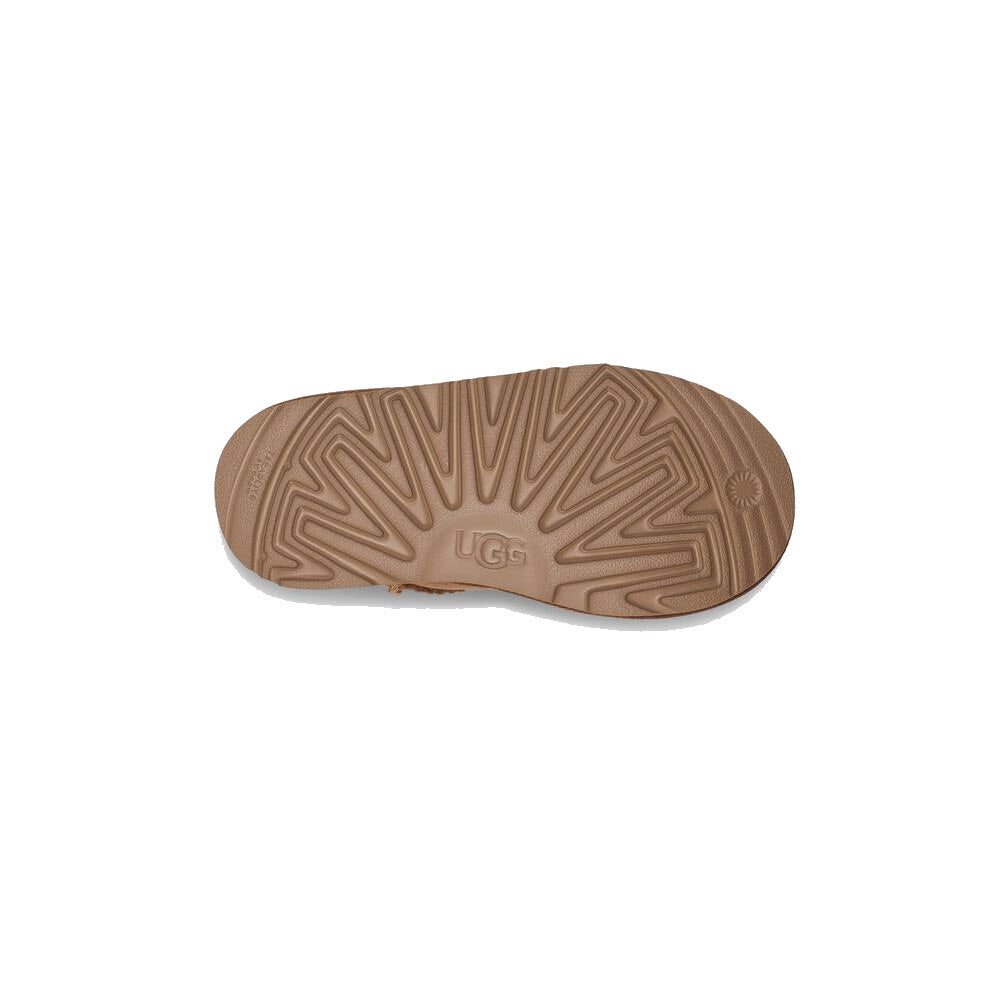 The image shows the sole of a brown Ugg UGG CLASSIC ULTRA MINI CHESTNUT - KIDS shoe, displaying a pattern with the Ugg logo in the center and hints of its cozy sheepskin lining ideal for all-day play.