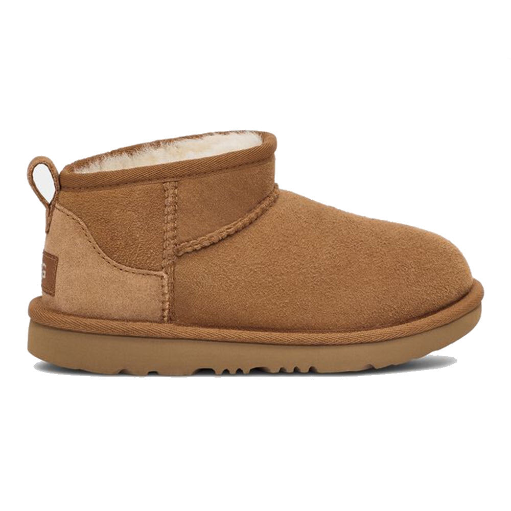 An UGG CLASSIC ULTRA MINI CHESTNUT - KIDS tan suede ankle boot with a thick sole, a pull tab at the back, and a cozy sheepskin lining perfect for all-day play by Ugg.