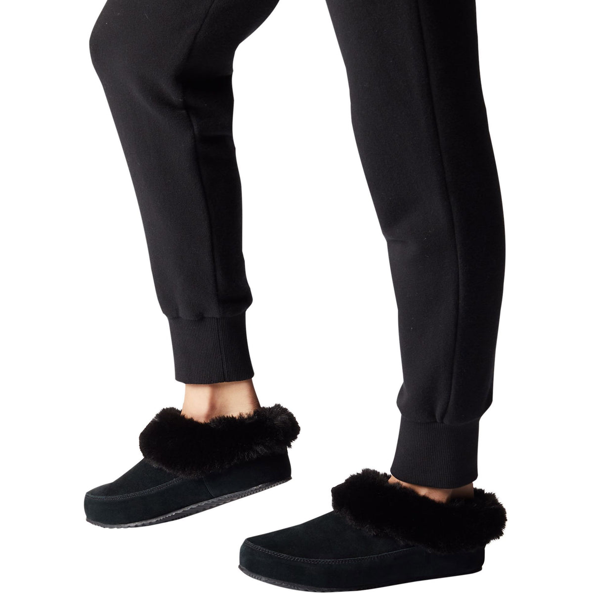 A person is shown from the ankles down, wearing black sweatpants and a pair of SOREL GO COFFEE RUN BLACK - WOMENS slippers by Sorel, which are luxuriously soft with a tough sole, perfect for quick trips outside.