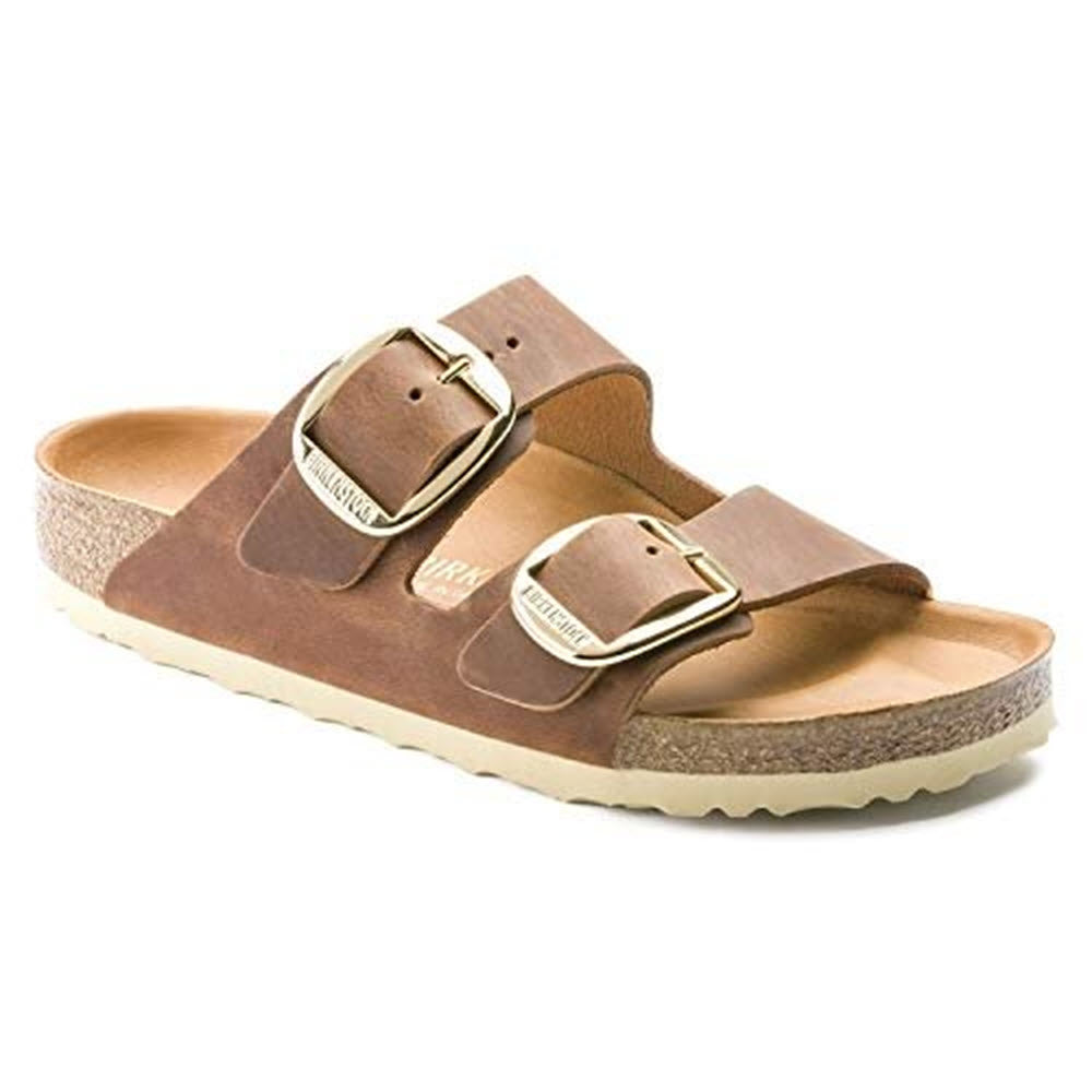 The BIRKENSTOCK ARIZONA BIG BUCKLE COGNAC OILED - WOMENS by Birkenstock features a two-strap design with adjustable straps, each adorned with a gold-tone buckle, and a beige sole.