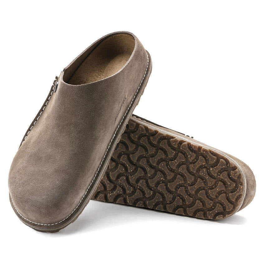 A pair of BIRKENSTOCK ZERMATT 365 GRAY TAUPE - WOMENS with suede lining and a textured sole, shown with one shoe standing upright and the other leaning against it.