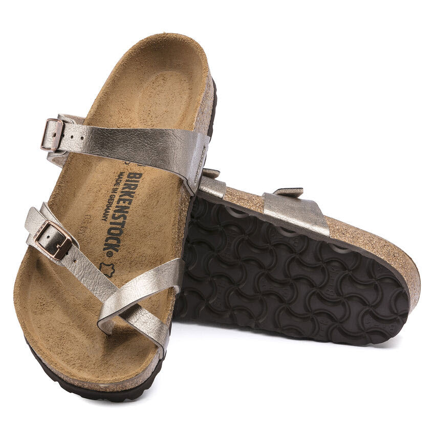 A pair of metallic silver Birkenstock BIRKENSTOCK MAYARI GRACEFUL TAUPE BIRKOFLOR - WOMENS sandals with cork footbeds and black textured rubber soles. The comfortable sandal features adjustable straps with metal buckles. One sandal is laid on its side, partially overlapping the other.