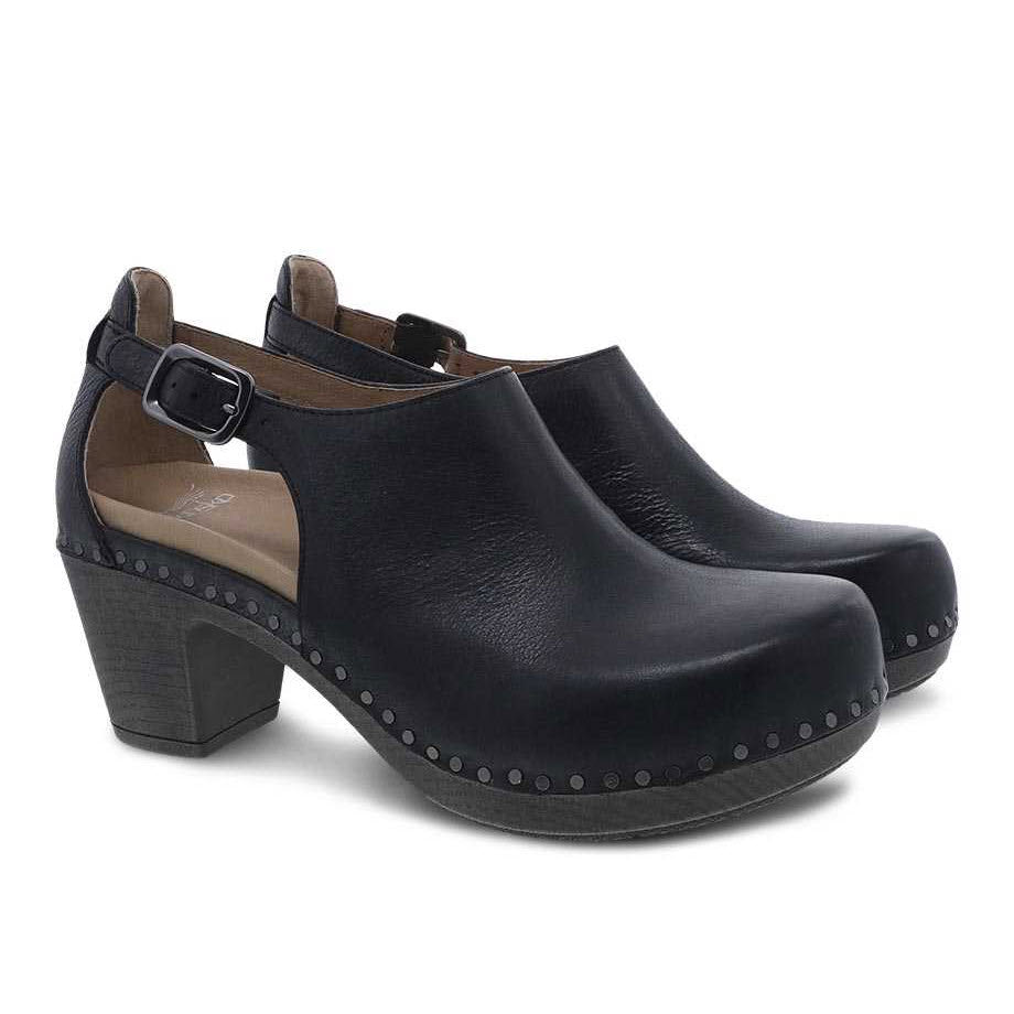 A pair of DANSKO SASSY BLACK - WOMENS from Dansko with nubuck uppers, a buckle strap, and stud detailing along the bottom edge, featuring an EVA footbed for comfort. This transitional shoe is perfect for various occasions.