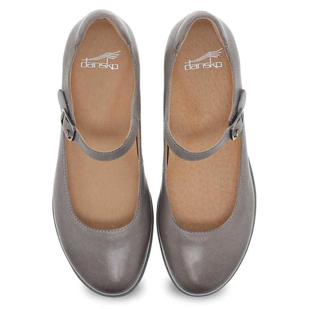 A top view of a pair of Dansko Marcella Taupe Burnished women&#39;s shoes, showcasing gray leather Mary Jane styling with buckles, a hidden wedge heel, and Dansko Natural Arch technology, all set against a white background.