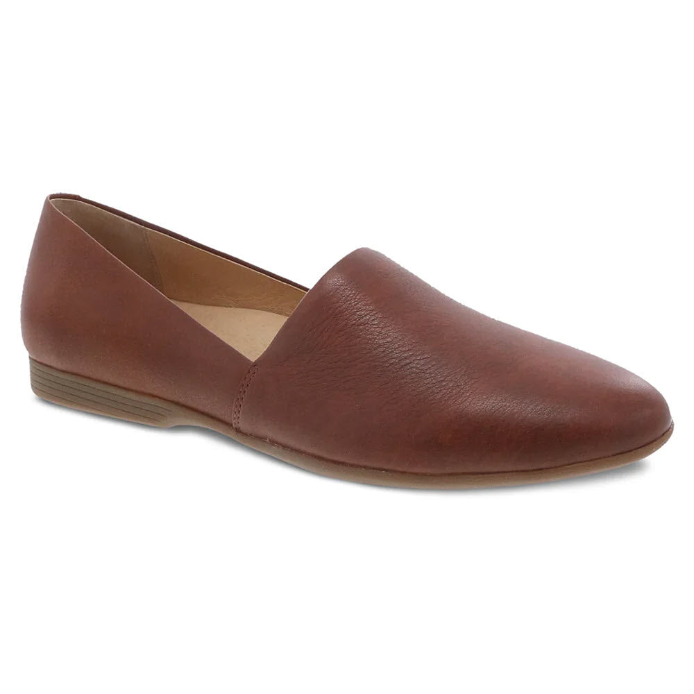 The Dansko Larisa Saddle for women is a brown leather flat shoe featuring a simple, slip-on design with leather uppers and a low heel.