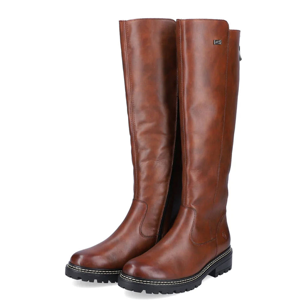 The REMONTE LUG SOLE TALL BOOT TAN for women by Remonte is displayed against a white background. These tall tan leather boots feature black rubber soles, a sleek design with visible stitching, and a side zip closure for easy wear.