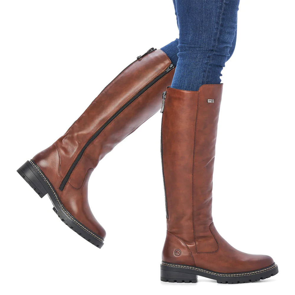 Person wearing REMONTE LUG SOLE TALL BOOT TAN by Remonte with dark-soled heels and side zip closure, paired with blue jeans.