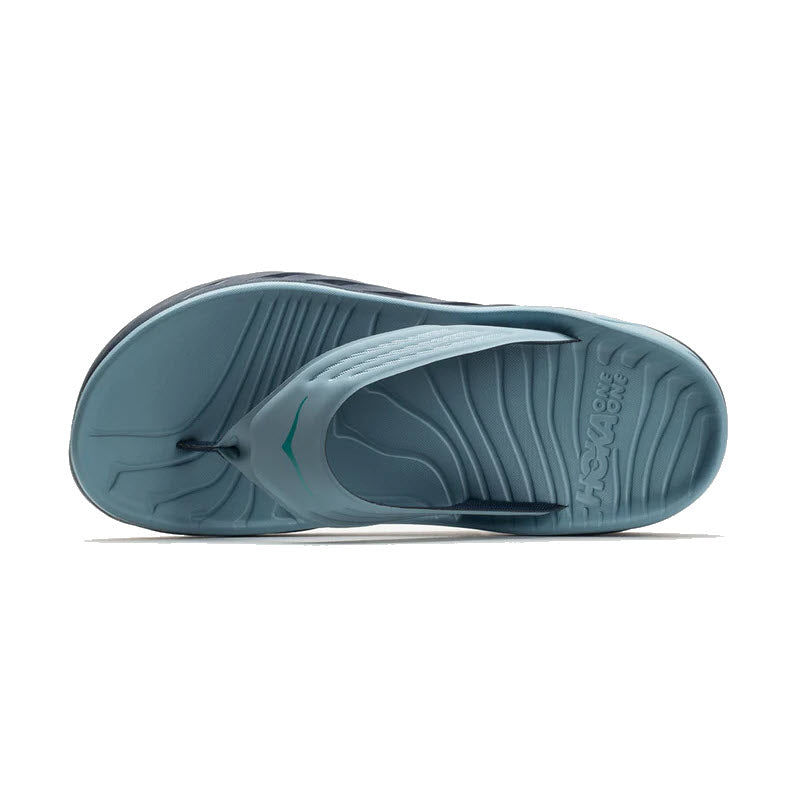 Blue &quot;HOKA ORA RECOVERY FLIP STONE BLUE/OUTER SPACE - MEN&quot; sandal viewed from above, showcasing a textured footbed and the Hoka brand name embossed on the sole. Features soft cushioning for added comfort and support throughout your day.