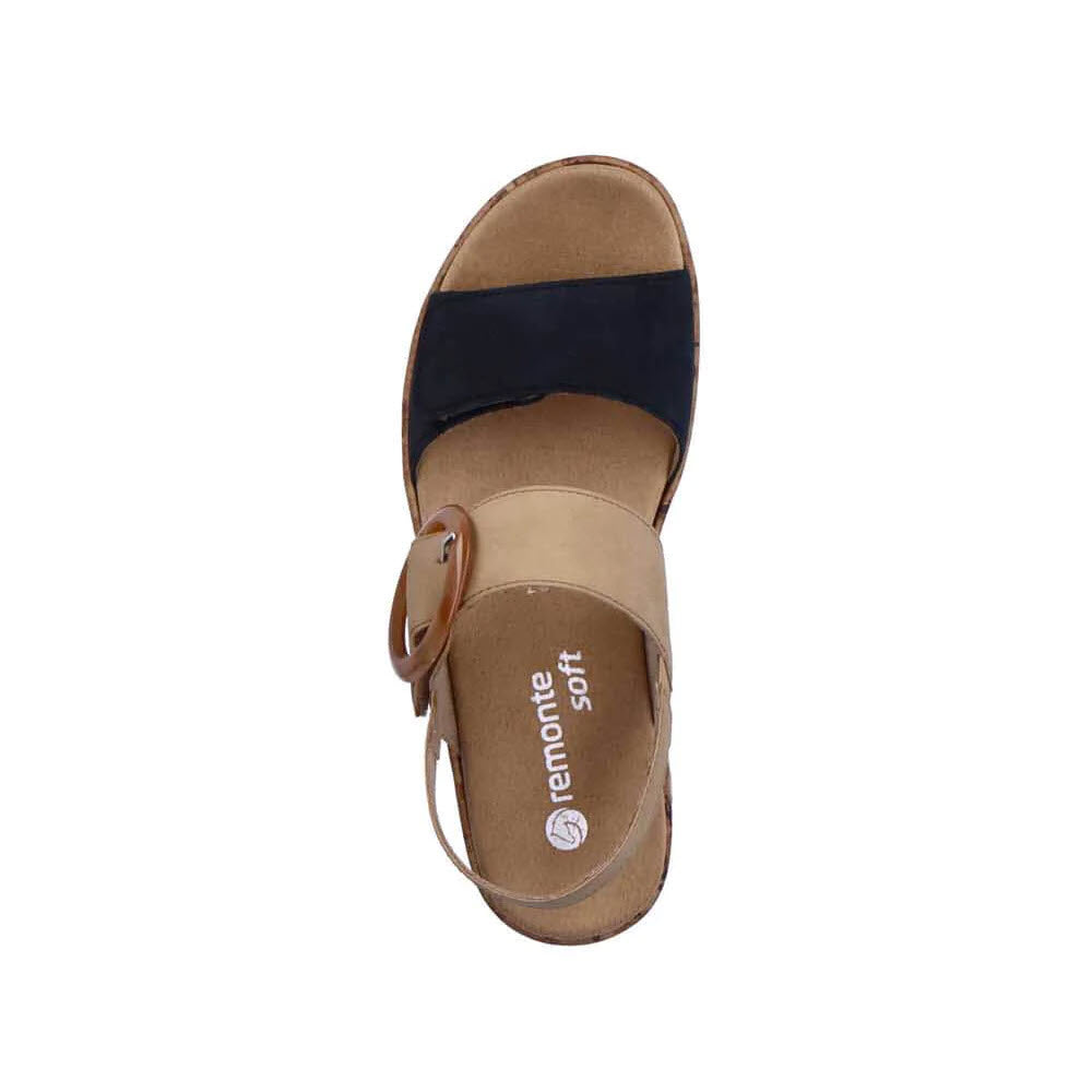 The Remonte Comfort Big Buckle Sandal in Black/Tan for women features a large buckle on the side and &quot;remonte soft&quot; inscribed on the insole, making it an ideal choice for those seeking comfort with a stylish design. This chic wedge sandal also includes adjustable straps for a custom fit.