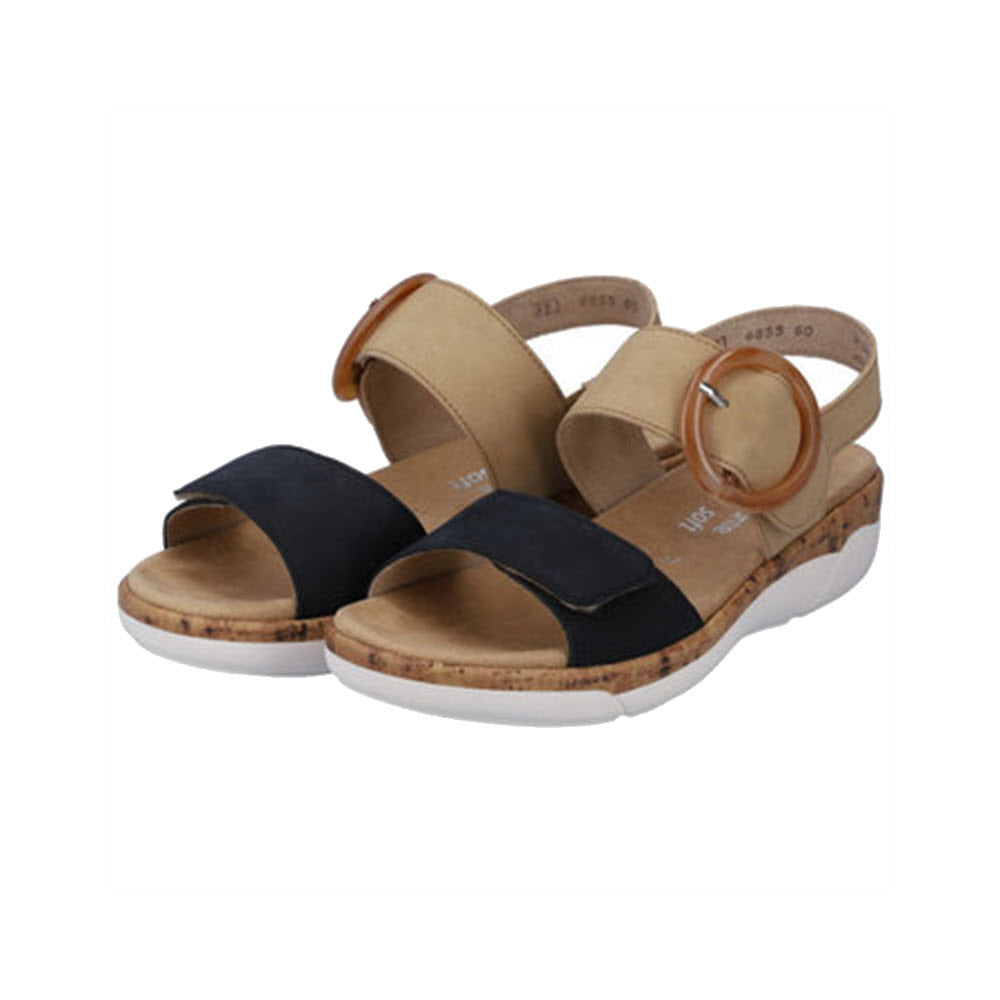 A pair of Remonte Comfort Big Buckle sandals for women featuring black and tan straps, cork soles, and white rubber outsoles. These Remonte sandals have large brown circular buckles on the adjustable ankle straps.