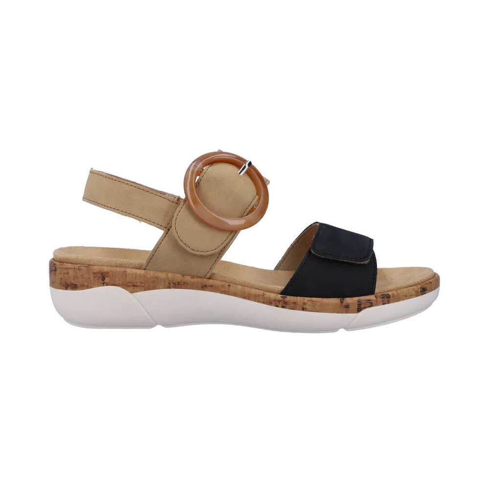 A Remonte REMONTE COMFORT BIG BUCKLE SANDAL BLACK/TAN - WOMENS with a tan and black leather upper, featuring a large circular buckle, adjustable straps, a white sole, and a low cork wedge heel.