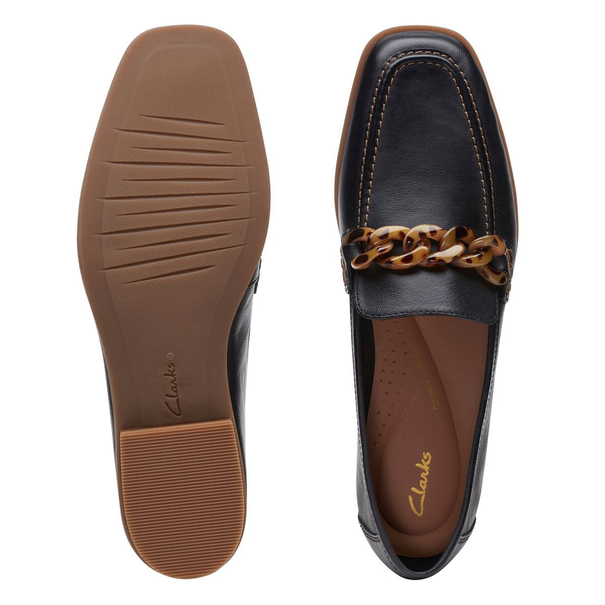 Pair of black Clarks Sarafyna Iris loafers for women, featuring brown undersoles, square toes, and a decorative vamp strap with a brown chain accent. One shoe is shown from the bottom and the other from the top.