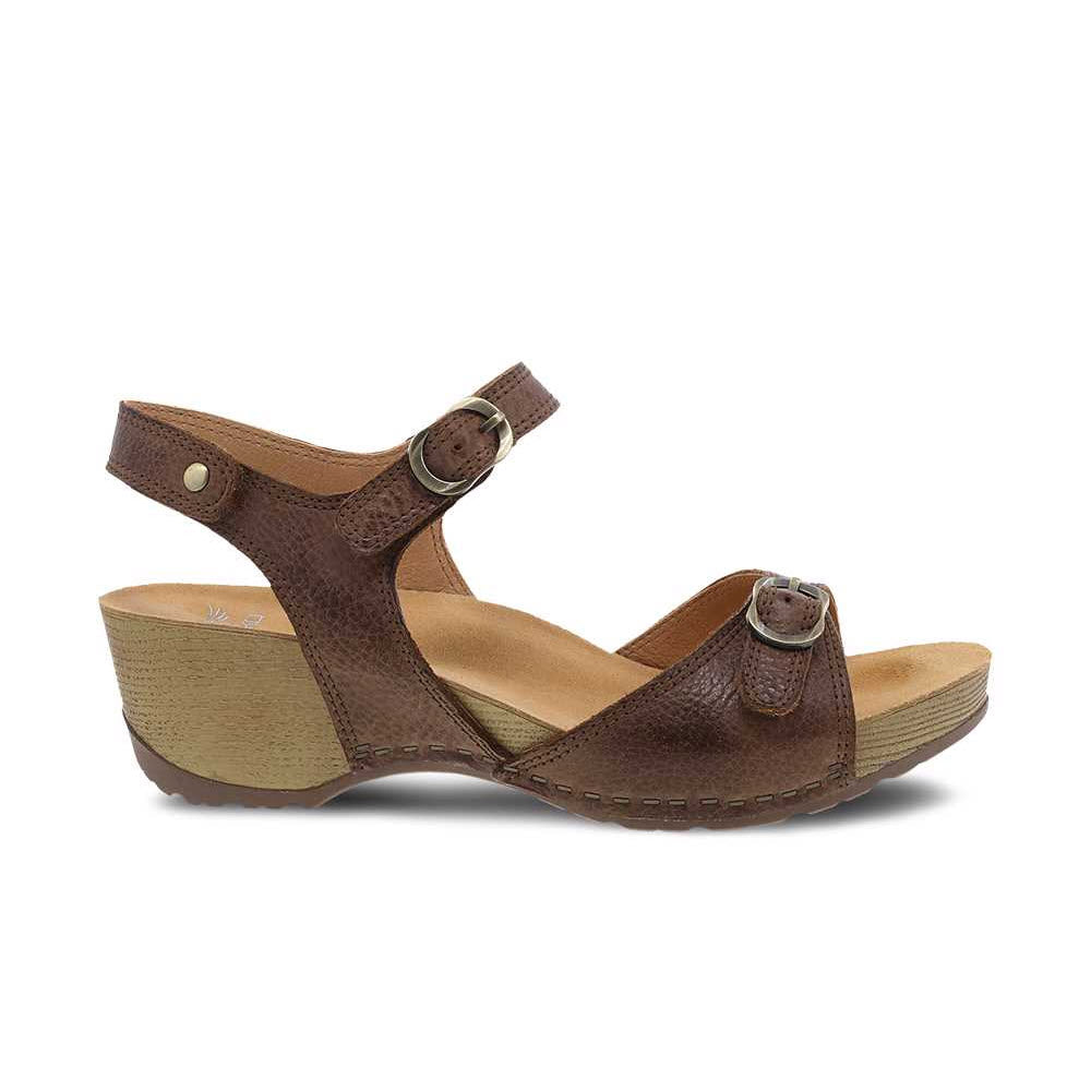 The DANSKO TRICIA BROWN - WOMENS by Dansko is a brown leather wedge sandal with an adjustable buckle strap over the foot and around the ankle. It features a cushioned insole and a textured outsole for premium comfort, making it perfect for warm weather.