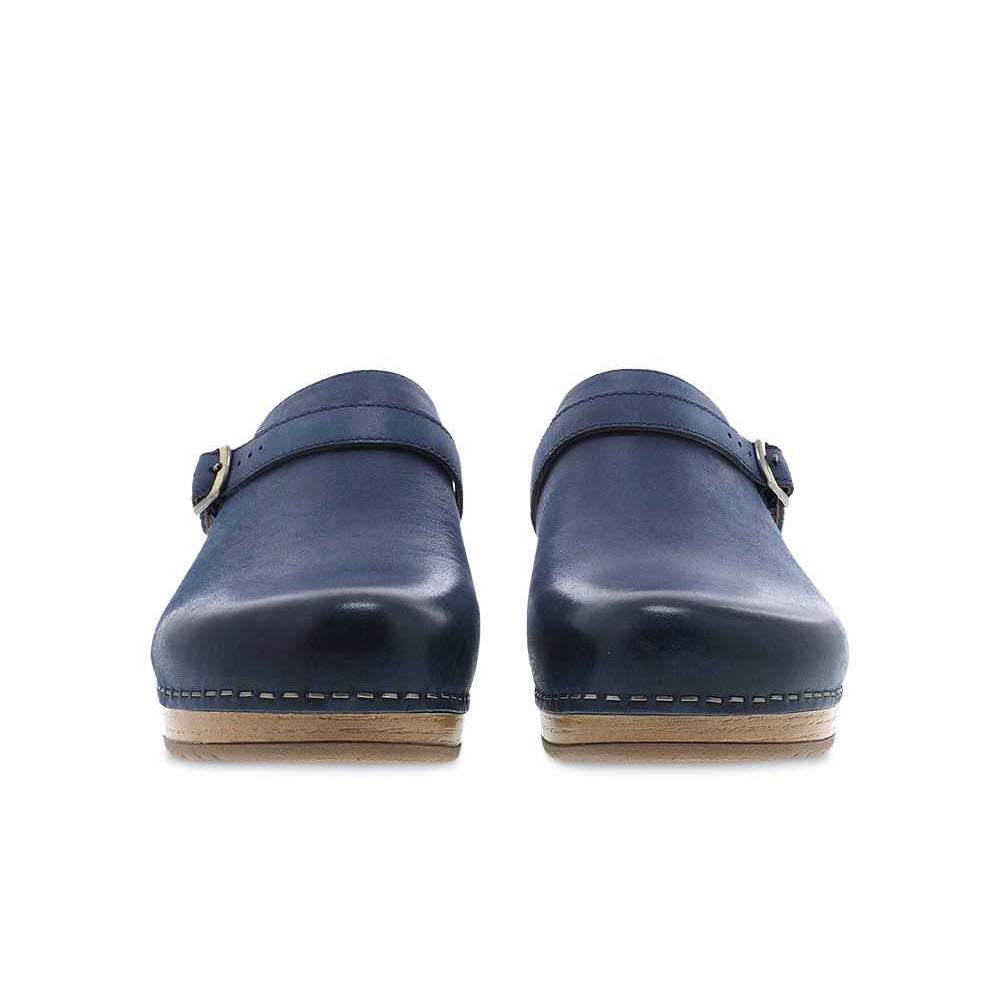 The DANSKO BERRY NAVY - WOMENS clogs from Dansko feature Nubuck leather uppers in a navy blue shade, an adjustable ankle strap, and a light wood sole when viewed from the front.