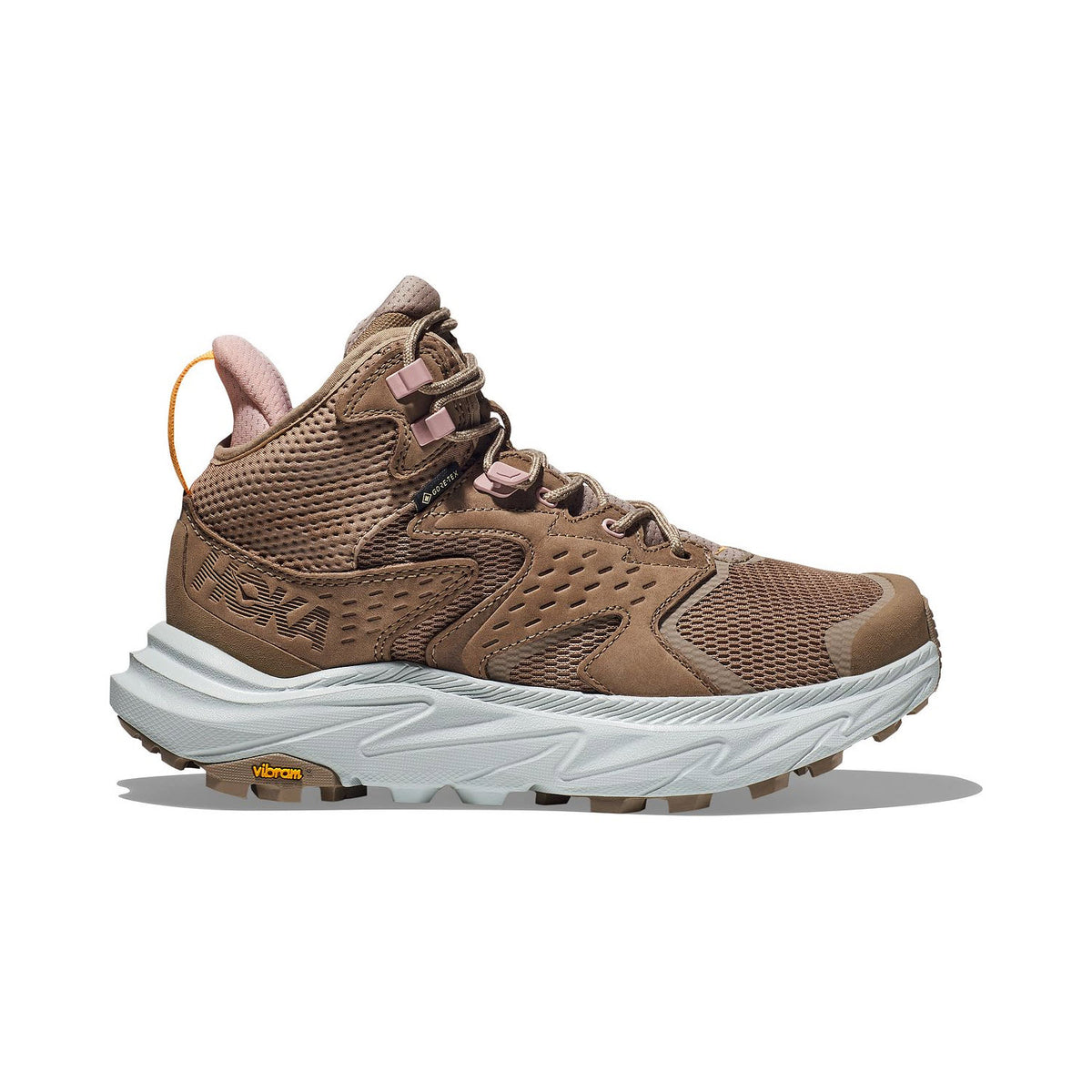 The HOKA ANACAPA 2 MID GTX DUNE/ICE FLOW - WOMENS by Hoka is a brown athletic hiking shoe featuring a thick white sole, ultra-ventilated mesh and synthetic upper, an ankle-high design, and lace-up closure. It is equipped with Vibram Megagrip branding on the sole for enhanced traction.